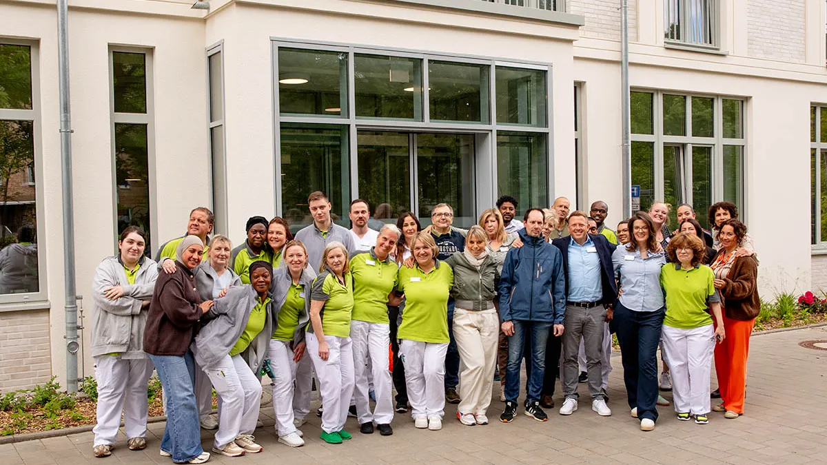 Eine gut gelaunte Gruppe von ungefähr 30 Mitarbeitern von PFLEGEN & WOHNEN UHLENHORST hat sich vor dem Gebäude aufgestellt.