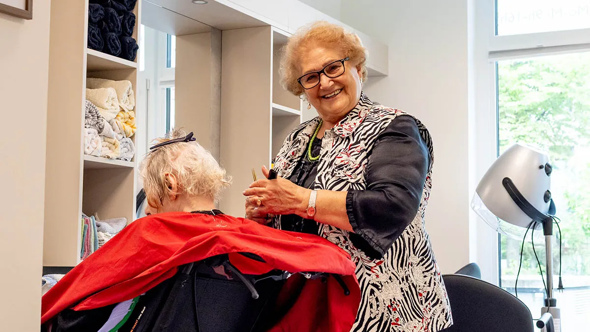 Eine Friseurin schneidet einer Seniorin die Haare im Friseursalon bei PFLEGEN & WOHNEN UHLENHORST.